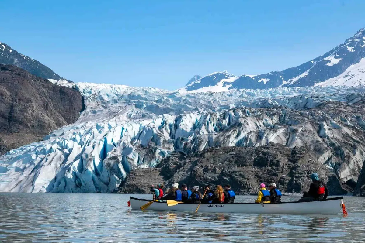 Paddlers landing their canoe on the moraine below the blue ice on a Mendenhall Glacier canoe paddle and hike tour